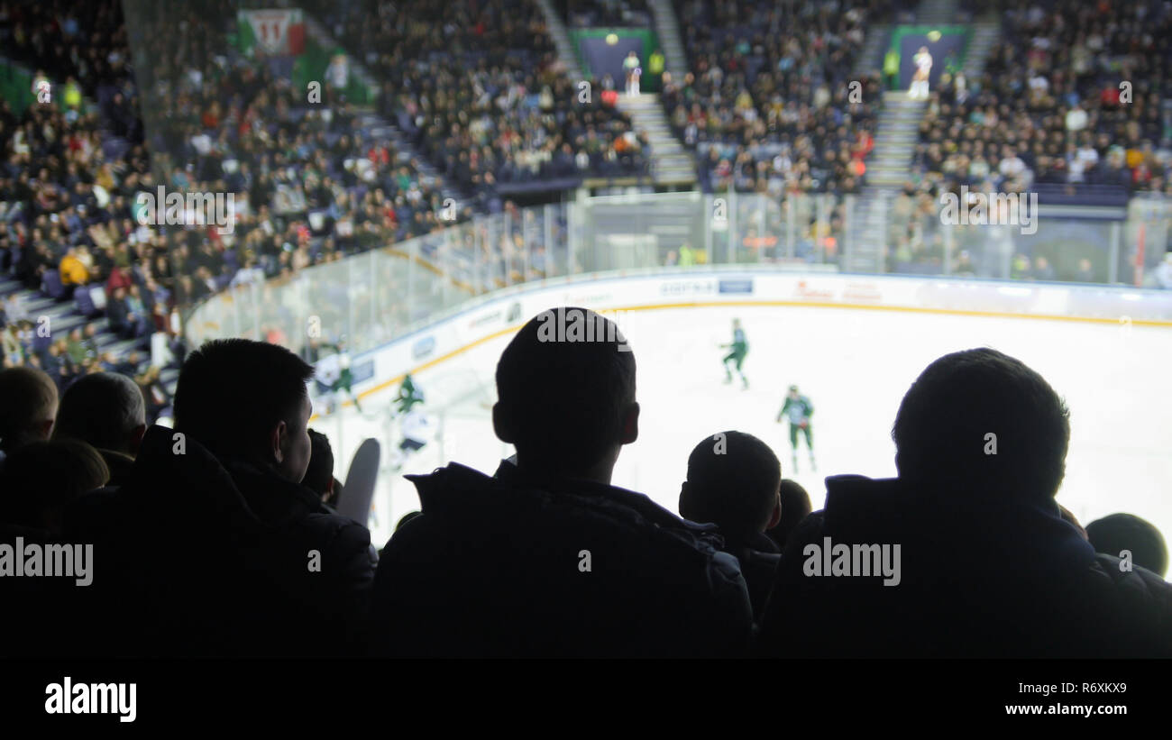 Un gruppo di sagome di giovani guardare la partita di hockey su ghiaccio in uno stadio chiuso Foto Stock