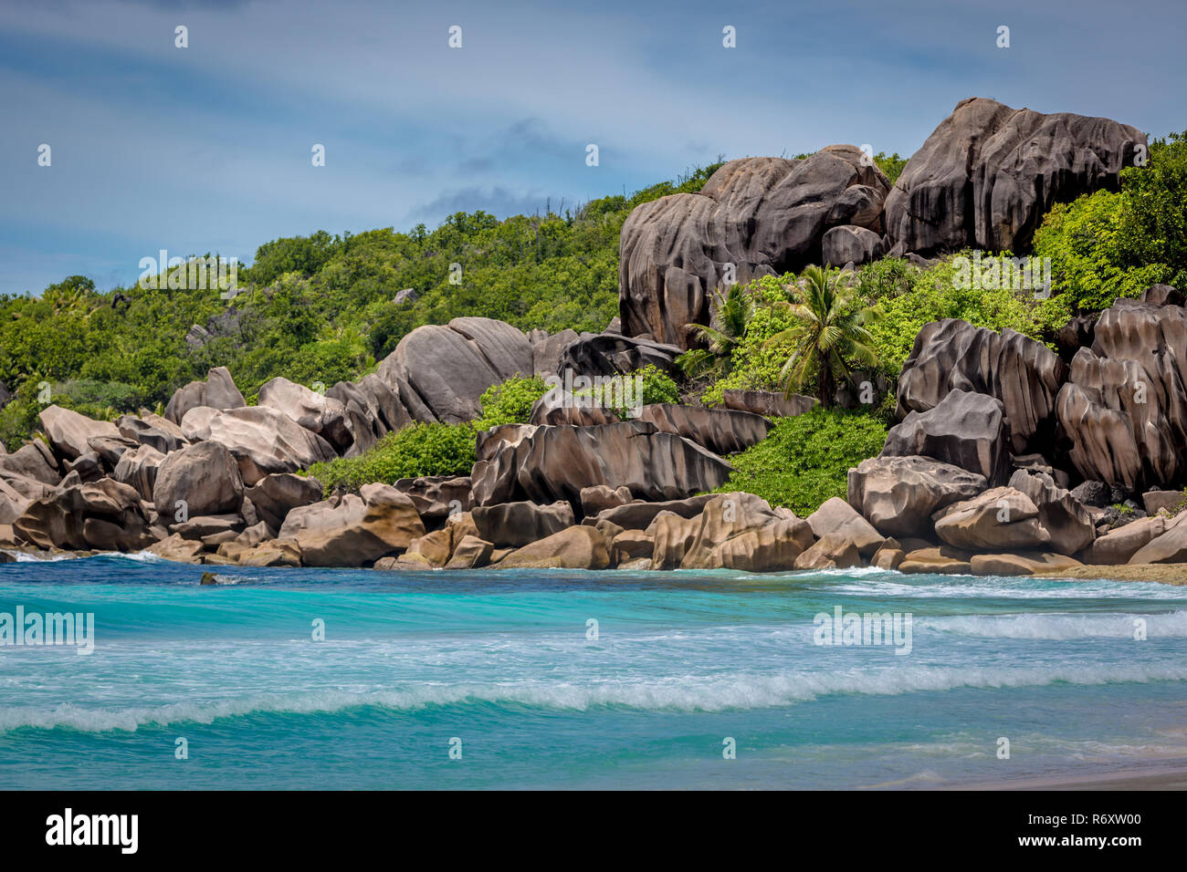 Spiaggia stupefacente scenario con acque blu del mare e unica forma di roccia tra il verde della vegetazione in Praslin alle Seychelles in un cielo blu giorno Foto Stock