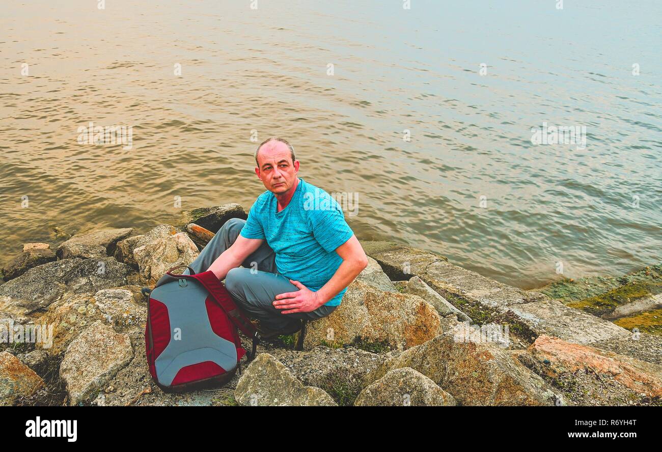 Midle invecchiato uomo seduto sulla riva del lago. Solitudine uomo maturo seduto sulla banca. Concetto di solitudine Foto Stock