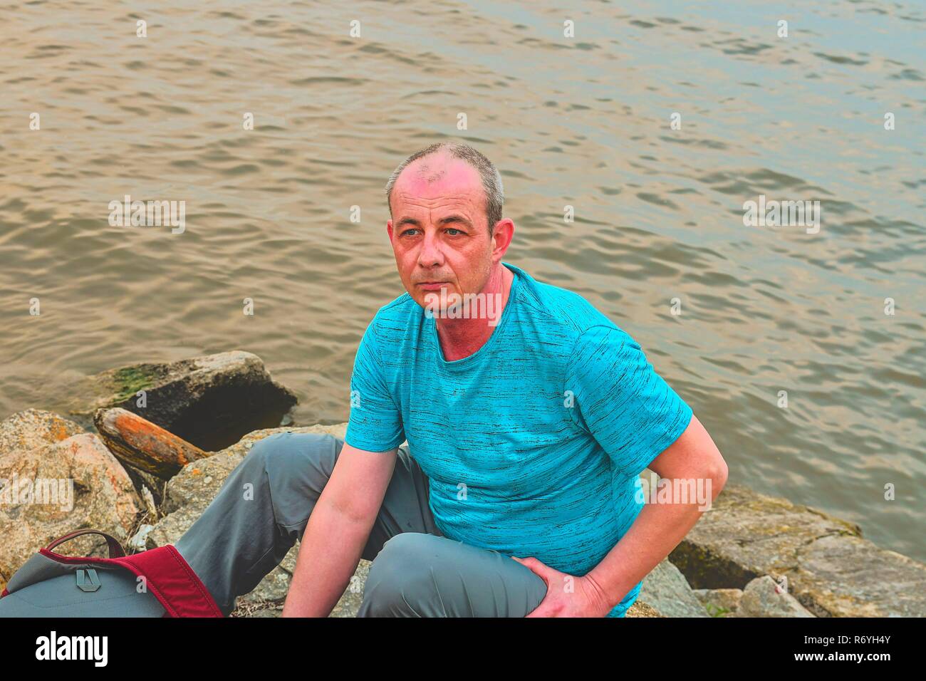 Midle invecchiato uomo seduto sulla riva del lago. Solitudine uomo maturo seduto sulla banca. Concetto di solitudine Foto Stock