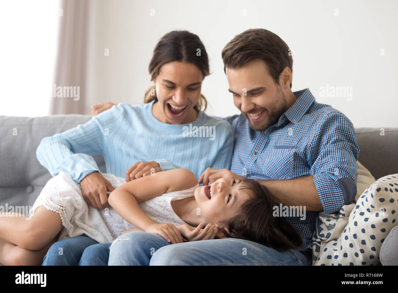 Il padre e la madre seduta sul lettino solletica giacente figlia Foto Stock