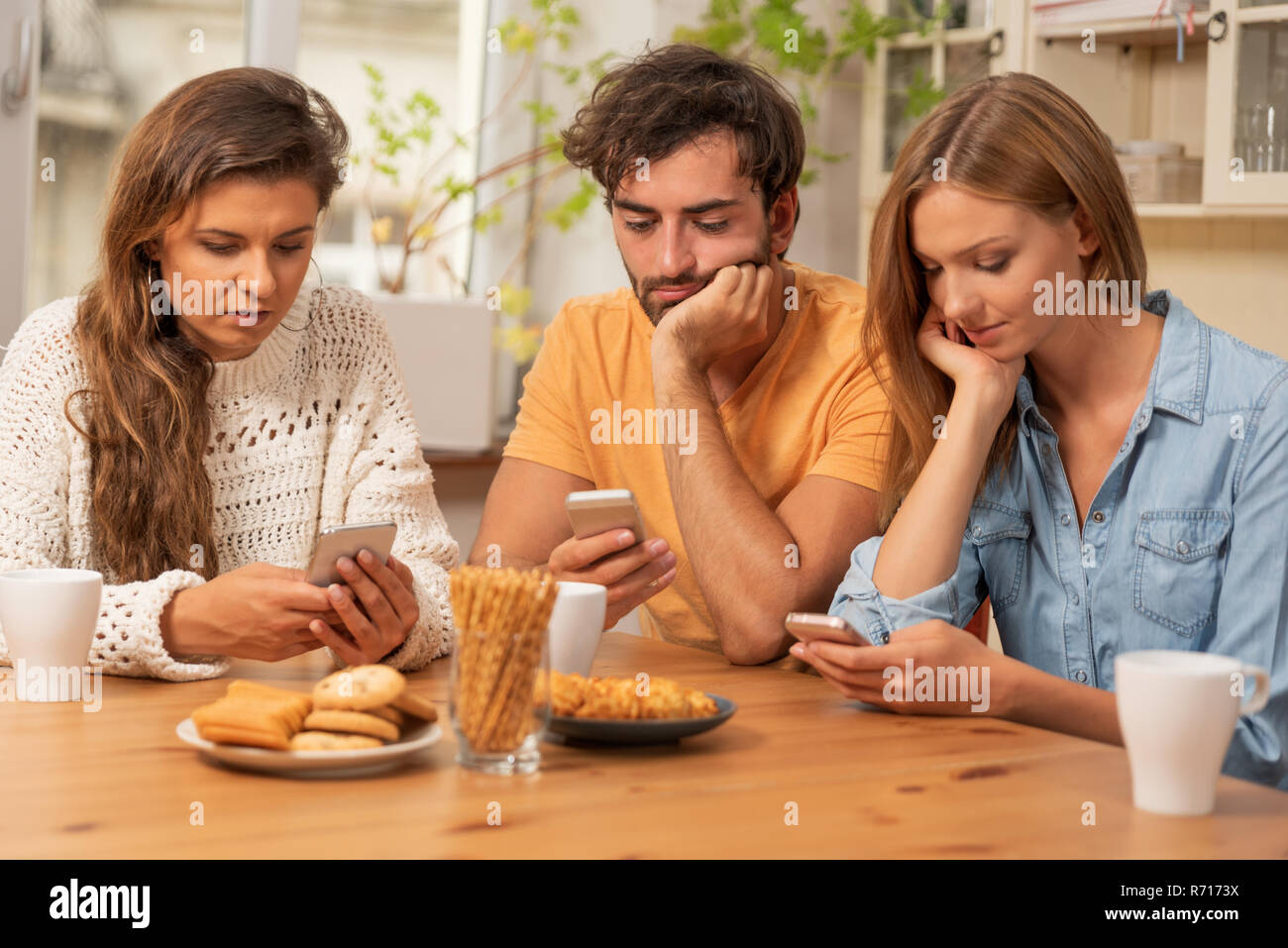 Amici seduti in cucina e guardare sui loro telefoni. La navigazione in Internet e la tecnologia concetto di dipendenza Foto Stock
