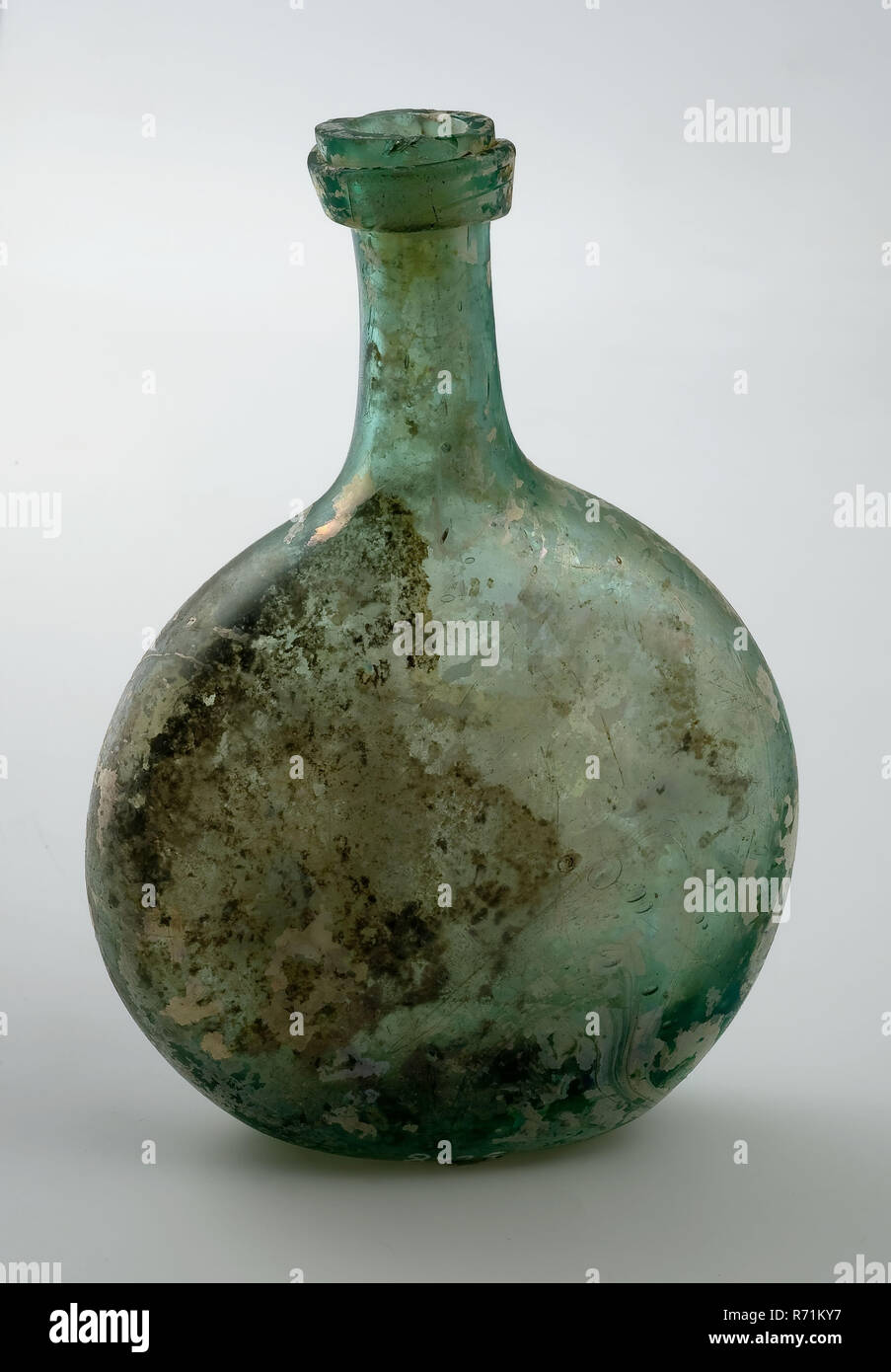 Piccolo verde bottiglia con corpo ovale e collo lungo, filo di vetro sotto il collo, portabottiglie suolo trovare vetro soffiato libero piccola bottiglia con collo lungo e ovale corpo piatto in chiaro vetro verde. Fondo appiattito con pontilemark circostante piana andando a filo di vetro sotto l'apertura del collo Irisation archeologia CONFEZIONAMENTO STOCCAGGIO DI TRASPORTO Foto Stock