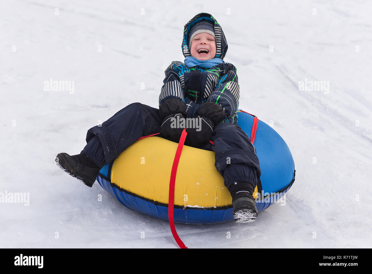 Allegro bello ragazzo a cavallo di un roller coaster. Il Toddler passeggiate nella neve in inverno. Il bambino ride e sorride in winter park. Foto Stock