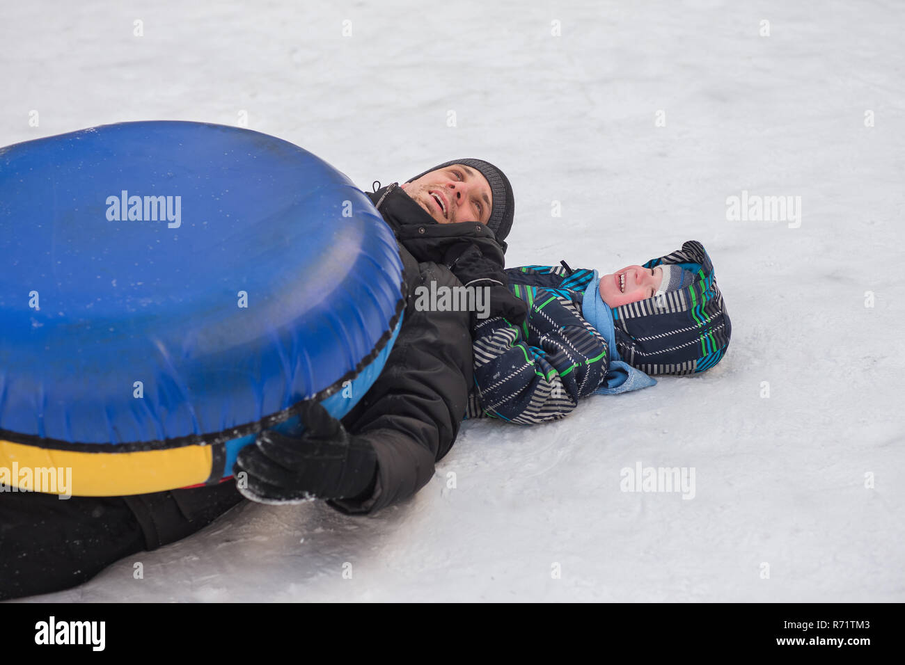 Un giovane uomo con un allegro ragazzo con un roller coaster ride in inverno sul ghiaccio. Bel Papà e figlio di ridere in un parco d'inverno. La famiglia felice giocare Foto Stock