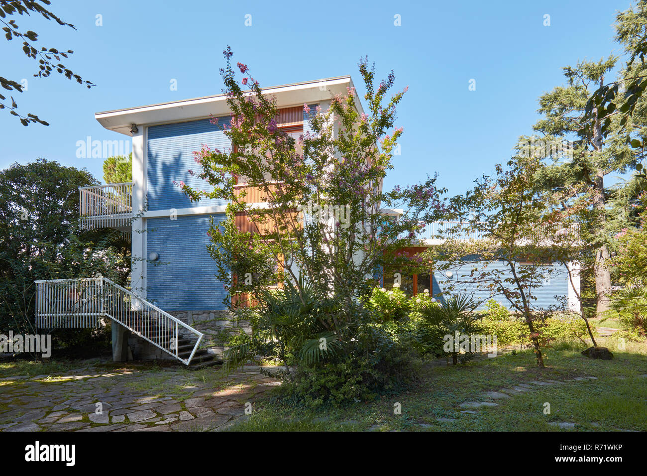 Villa con blu parete piastrellata e giardino in una soleggiata giornata estiva, cielo blu chiaro Foto Stock