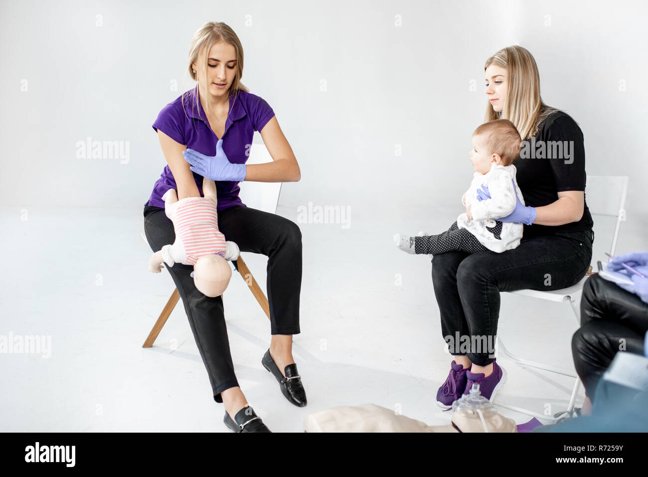 Giovane madre con bambino durante il primo aiuto alla formazione con istruttore che mostra sul manichino bambino come aiuto per la soffocante bambino Foto Stock