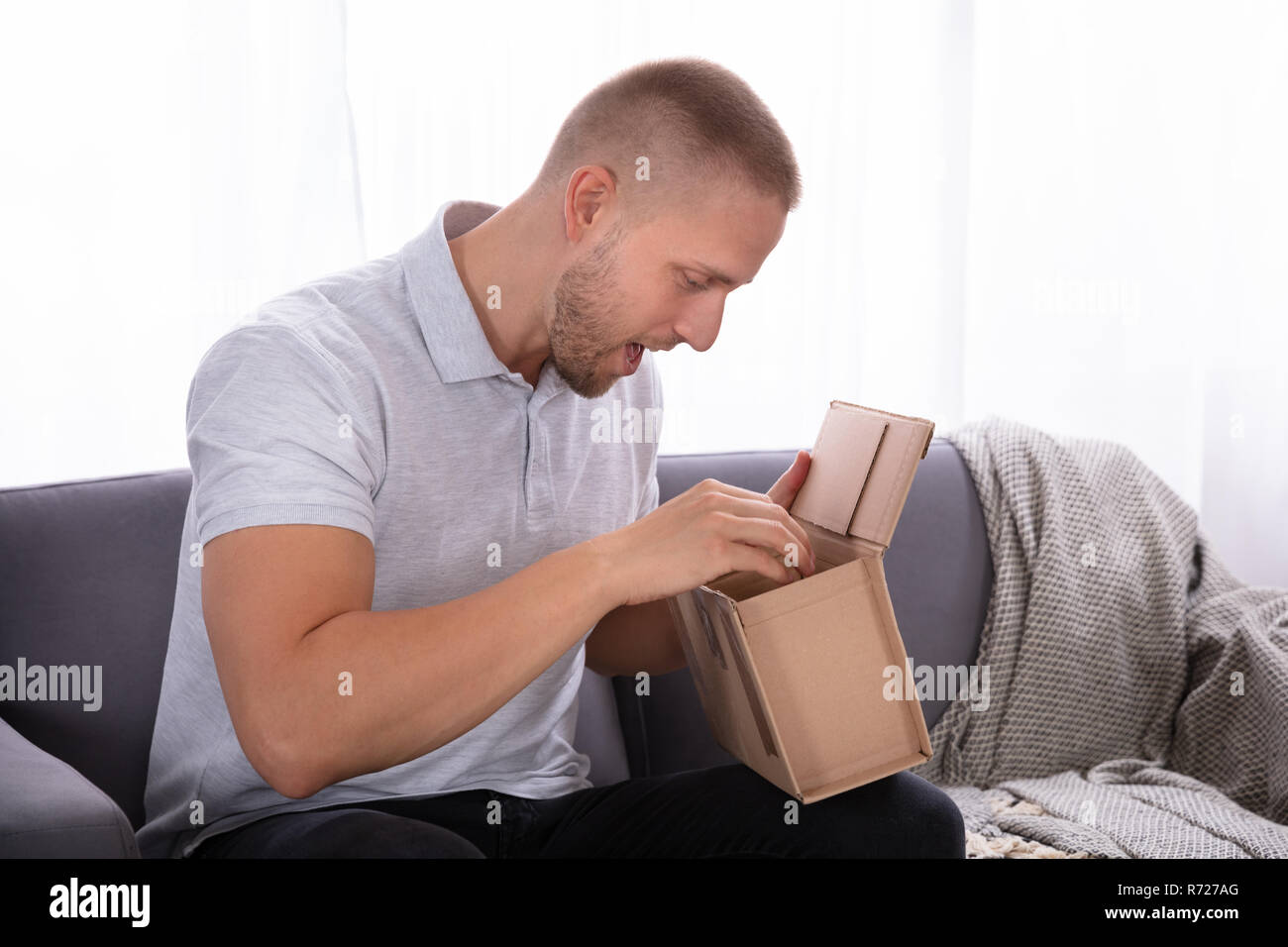 Giovane uomo seduto sul divano guardando all'interno consegnato il pacco Foto Stock