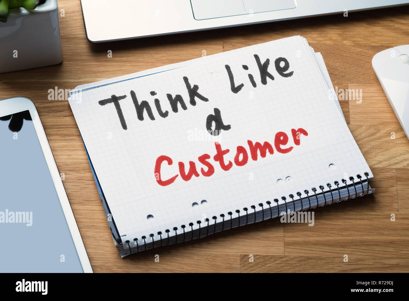 Pensare come un cliente testo scritto sul blocco note a spirale con gadget elettronici sulla scrivania Foto Stock