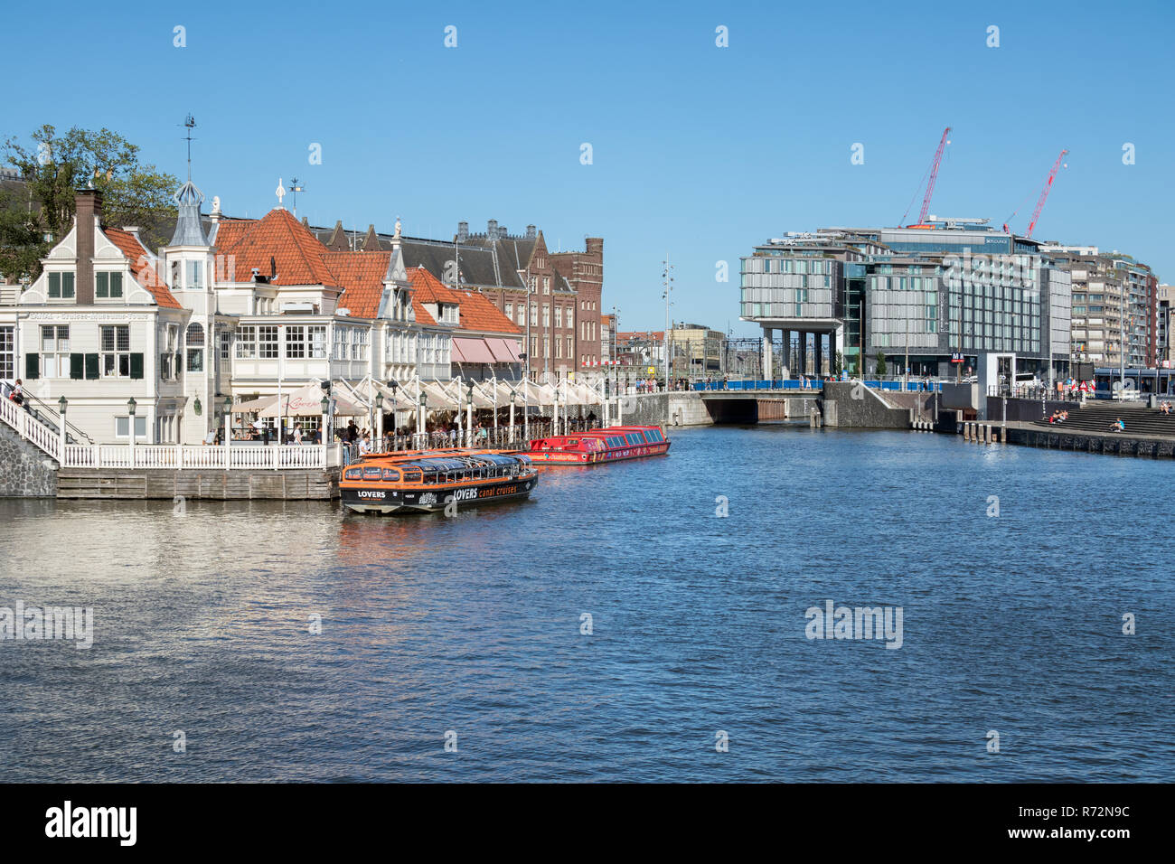 Canali di Amsterdam con lancia e edifici vicino stazione ferroviaria centrale Foto Stock