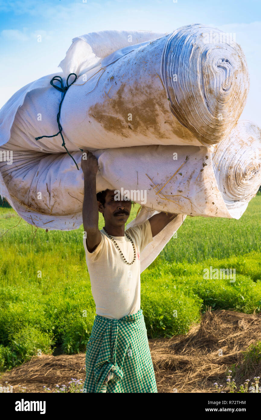 Uomo nepalese dal Tharu gruppo etnico portando grande rotolo in tessuto sulla sua testa, Chitwan, Nepal Foto Stock