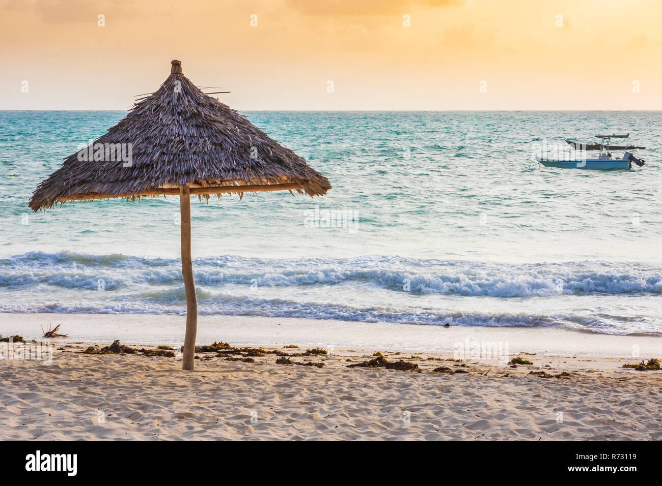 Ombrello di attrezzature per la spiaggia fatta di materiali naturali in una spiaggia tropicale al tramonto con il mare azzurro e sole effetto flare Foto Stock