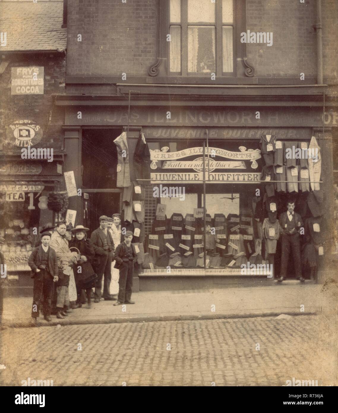 Edwardian fotografia di J.A.S(James) Illingworth capretti Outfitters, sarto e Clothier. 18 Attercliffe Road, Sheffield,South Yorkshire, Inghilterra, Regno Unito Assistenti / personale e clienti dal negozio di alimentari accanto hanno posto anche per la fotografia mentre il proprietario dei sarti mantiene un dignitoso e pongono unfunny. Circa 1905. Foto Stock