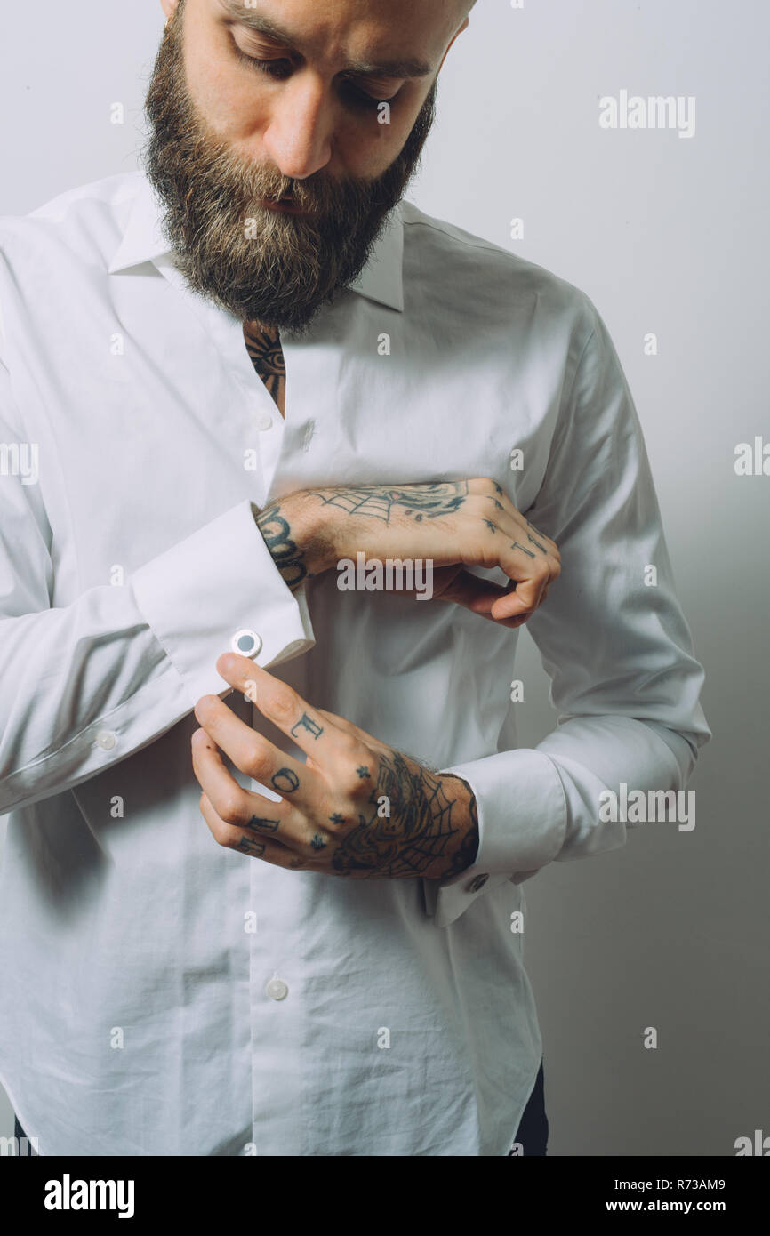 Barbuto giovane uomo che indossa una camicia bianca, facendo fino i gemelli, tatuaggi sulle mani Foto Stock
