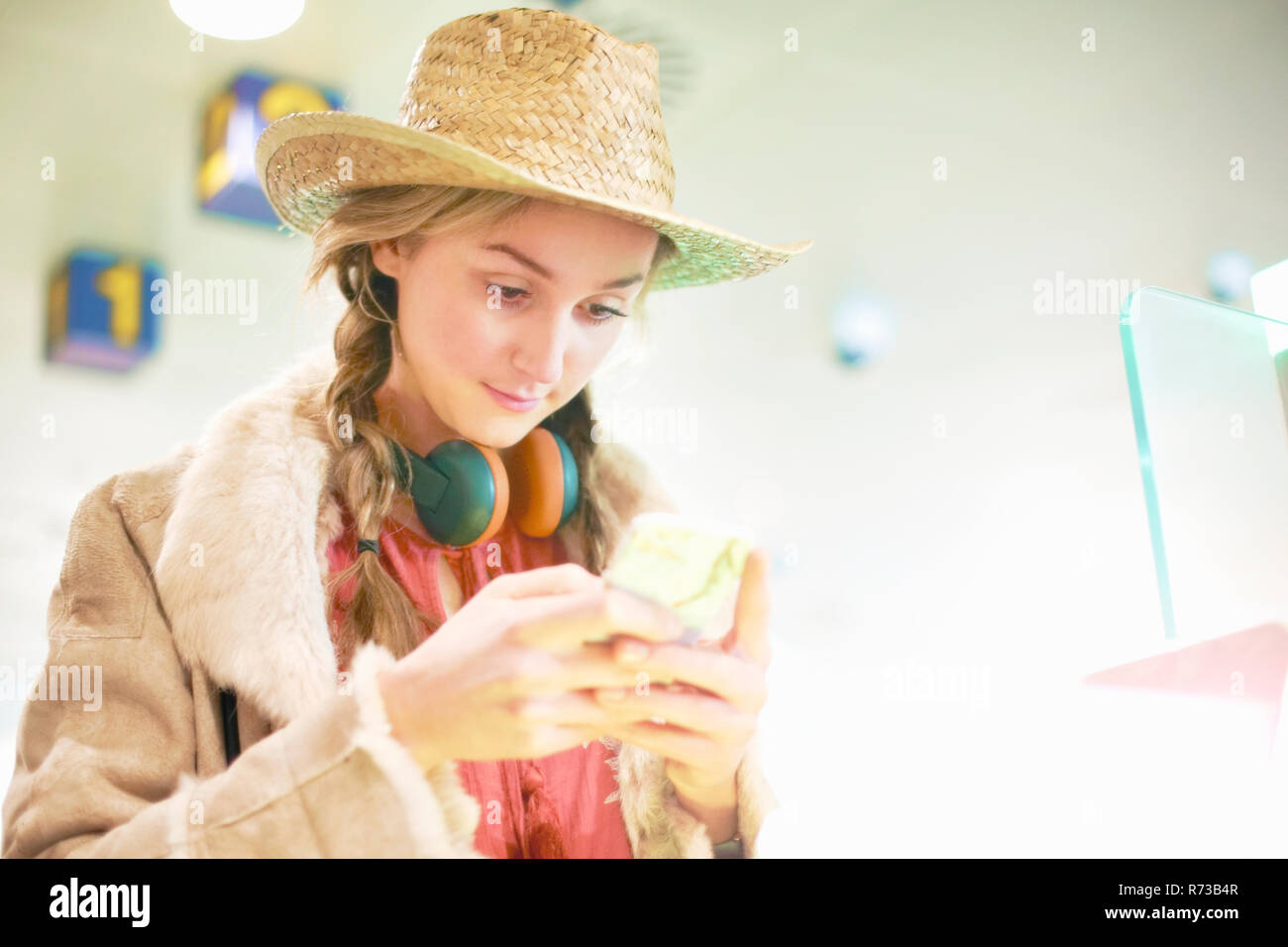 Giovane donna in aeroporto, utilizzando lo smartphone, le cuffie intorno al collo Foto Stock