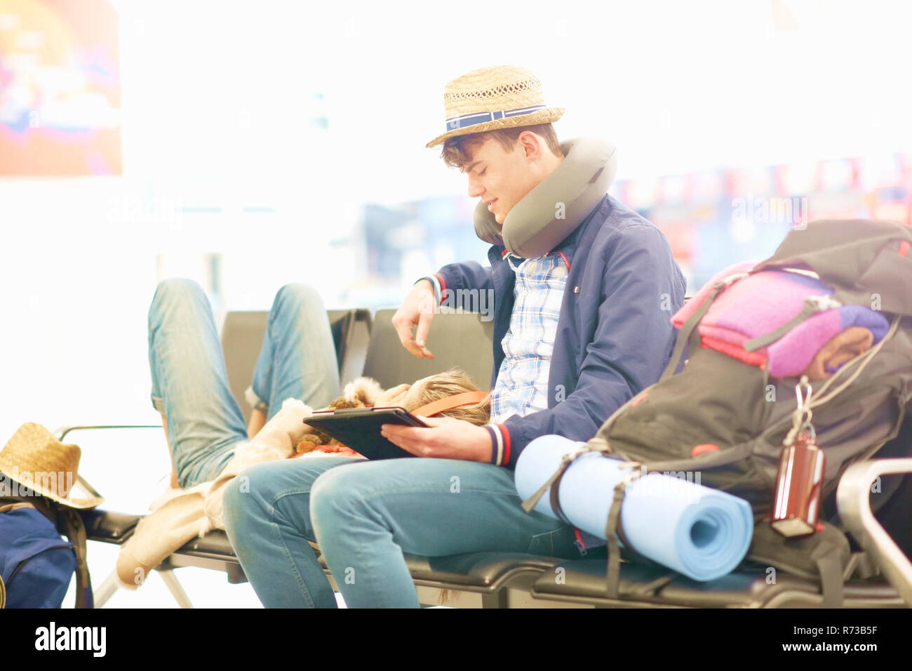 Coppia giovane in partenza lounge presso l'aeroporto, donna appoggiato la testa sull'uomo per le gambe, l'uomo con tavoletta digitale Foto Stock