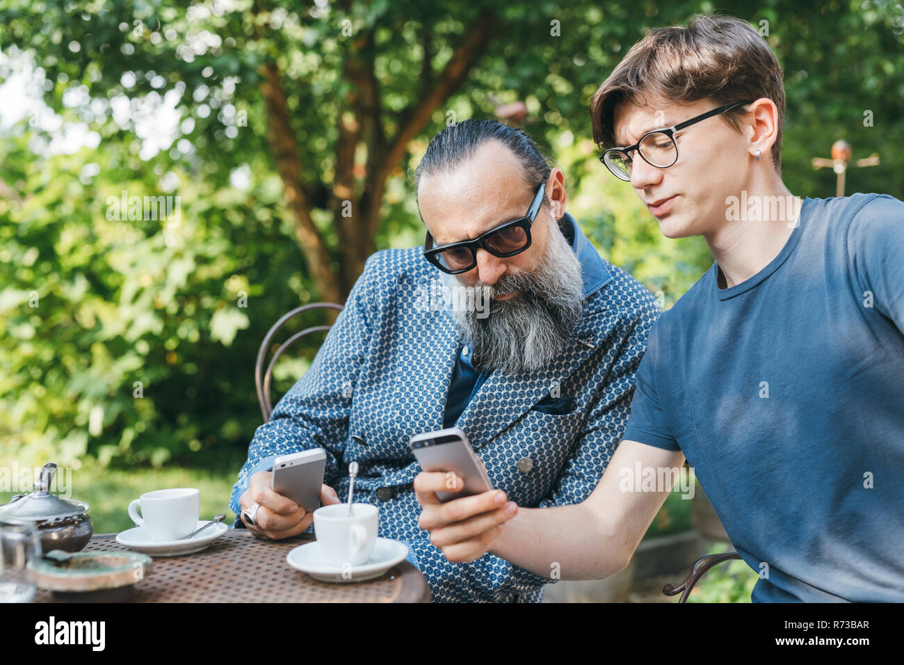 Uomo e figlio tramite cellulare in un caffè in giardino Foto Stock