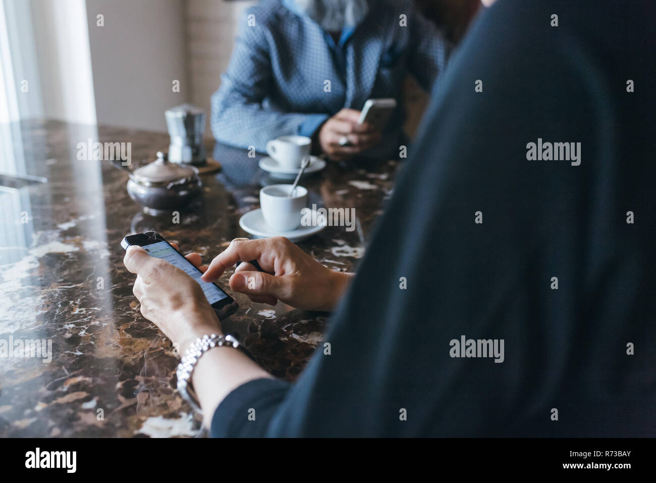 Giovane utilizzando il cellulare in un caffè in cucina Foto Stock