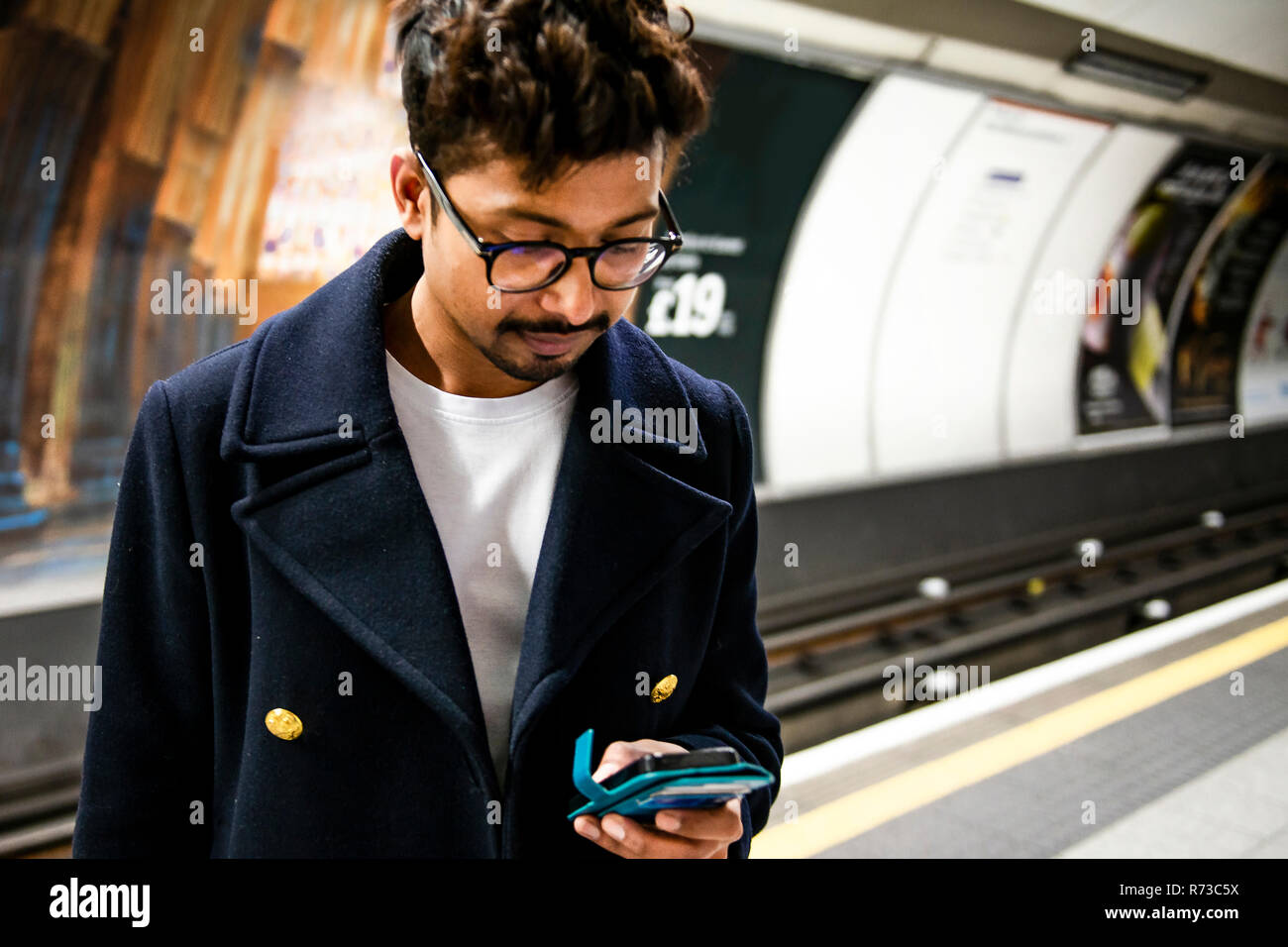 Imprenditore utilizza lo smartphone sulla piattaforma della stazione della metropolitana di Londra, Regno Unito Foto Stock