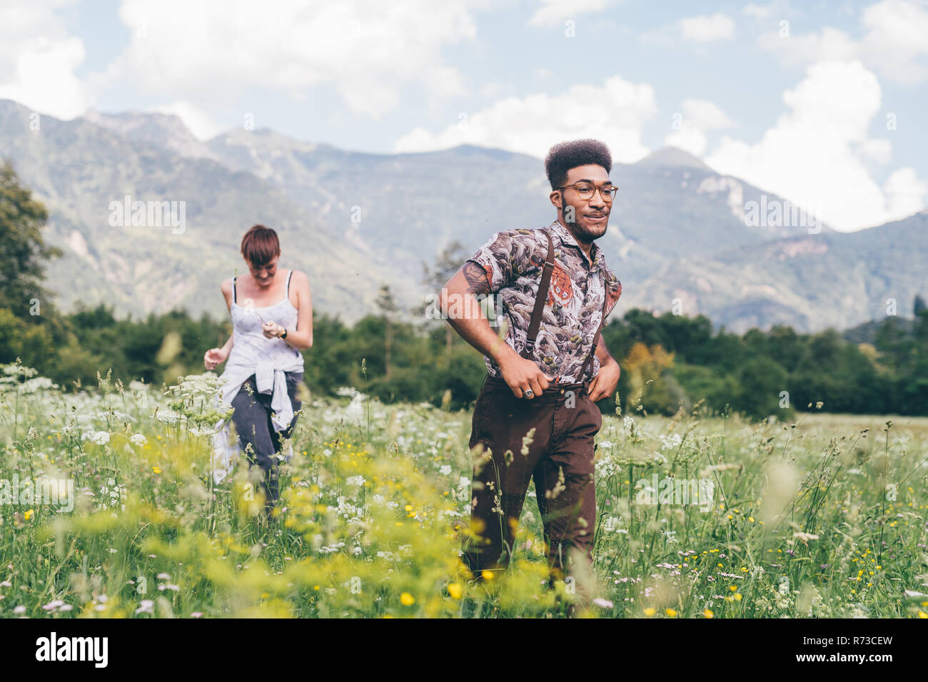 Giovane uomo e donna racing attraverso il prato di fiori selvaggi, Primaluna, Trentino-Alto Adige, Italia Foto Stock