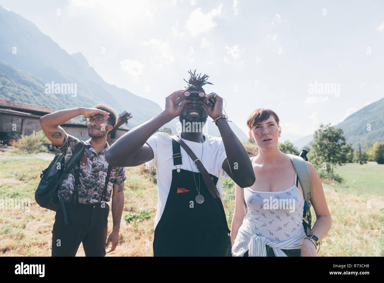 Tre giovani escursionismo amici cercando attraverso il binocolo da campo paesaggio, Primaluna, Trentino-Alto Adige, Italia Foto Stock