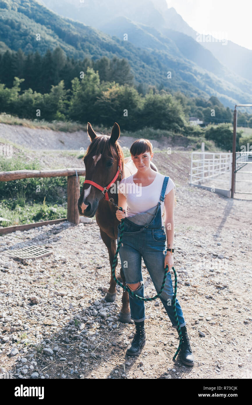 Giovane donna cavallo leader in rurale arena equestre a piena lunghezza ritratto Foto Stock