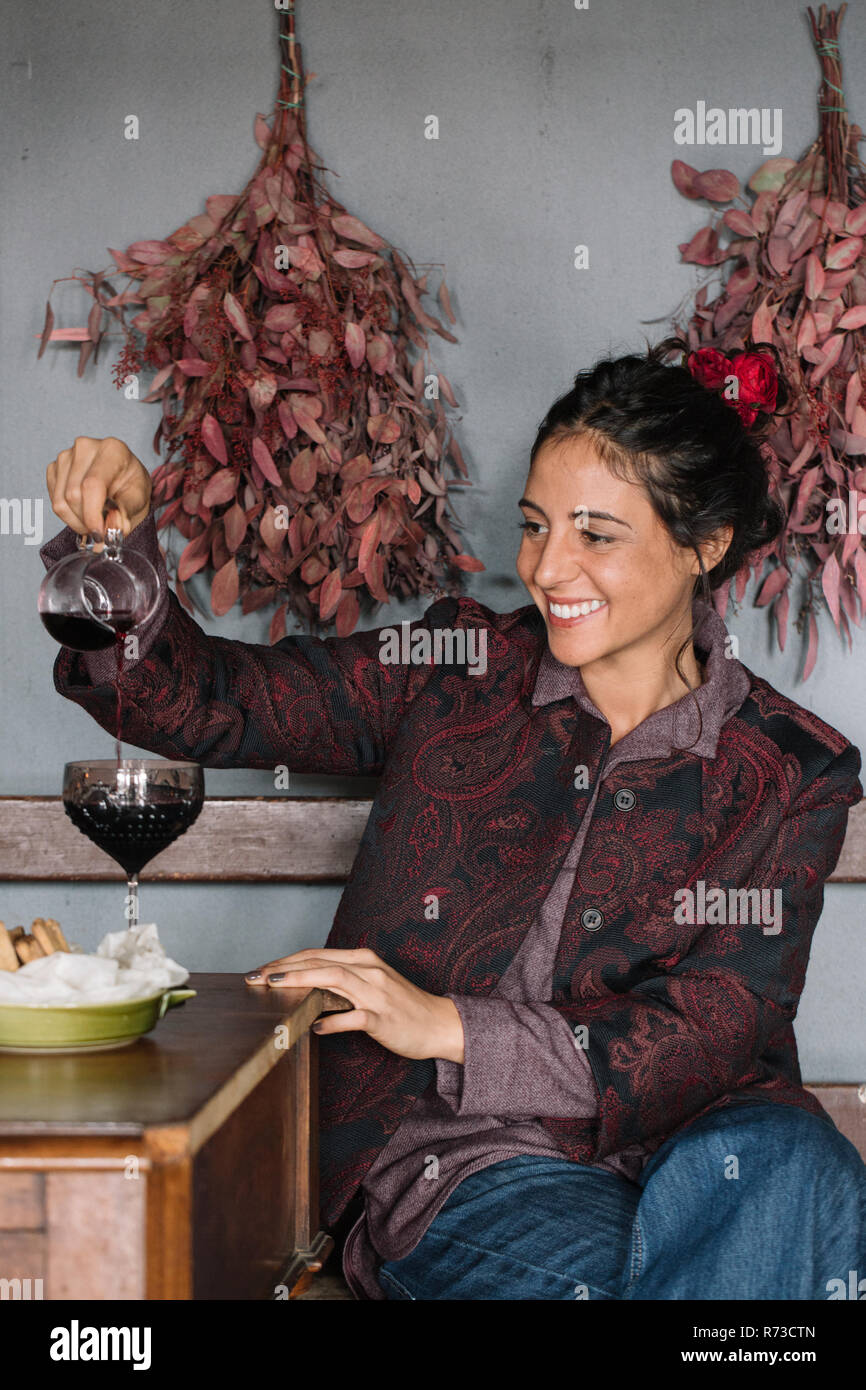 Giovane donna al tavolo rustico versando il vino rosso Foto Stock