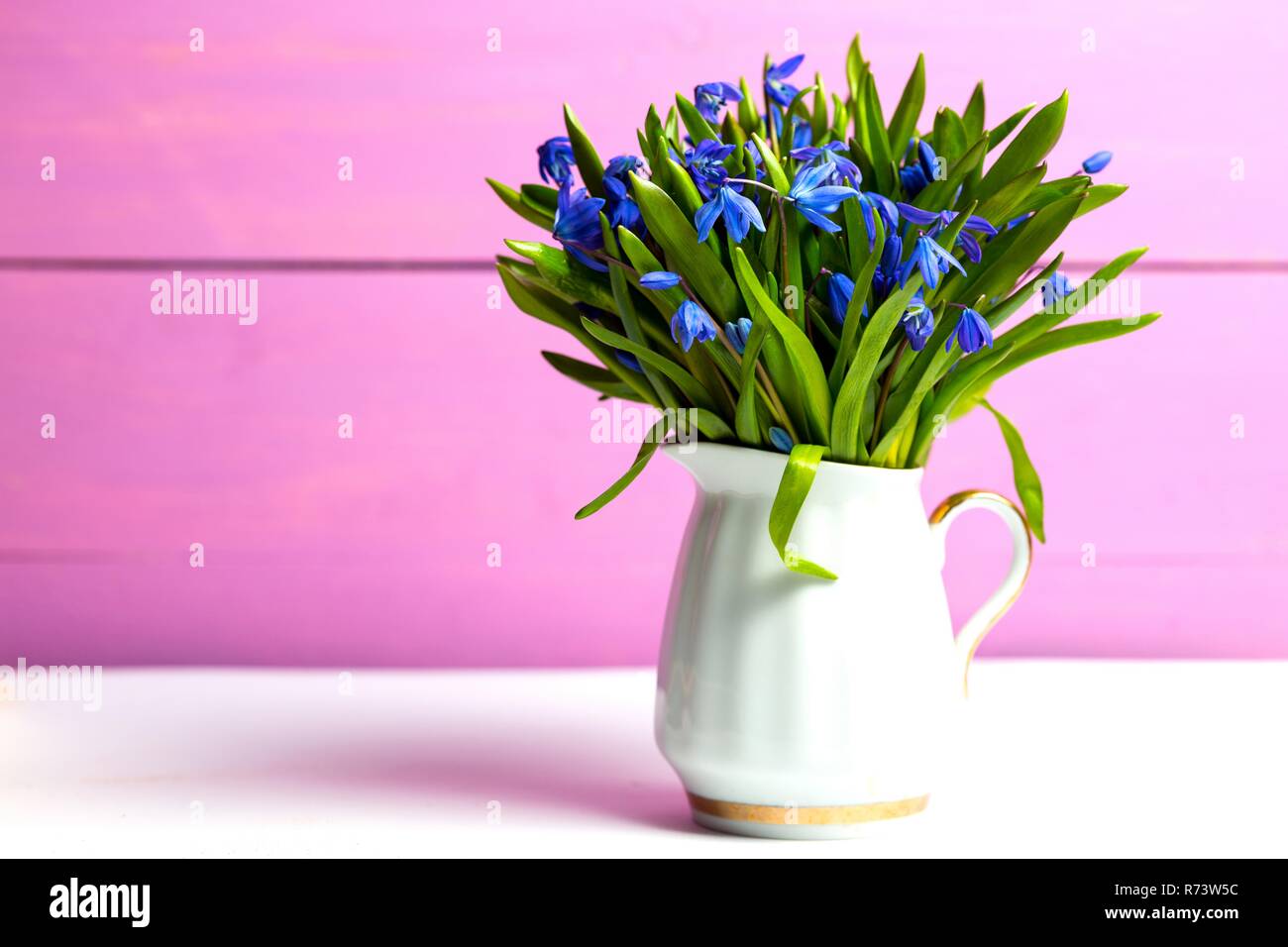 Snowdrops in un vaso su una tabella su un sfondo rosa Foto Stock