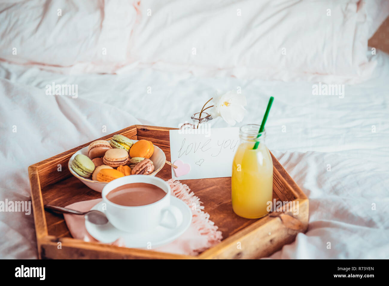 La prima colazione a letto con ti amo il testo di una nota. Tazza di caffè  o di cacao, succo, amaretti, rose fiore sul vassoio in legno Colazione  romantica a letto. Birt