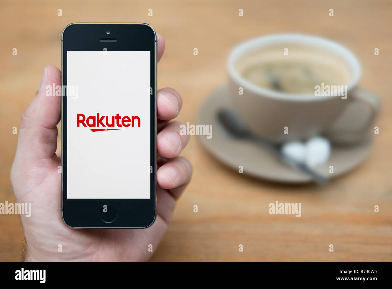 Un uomo guarda al suo iPhone che visualizza il logo Rakuten (solo uso editoriale). Foto Stock