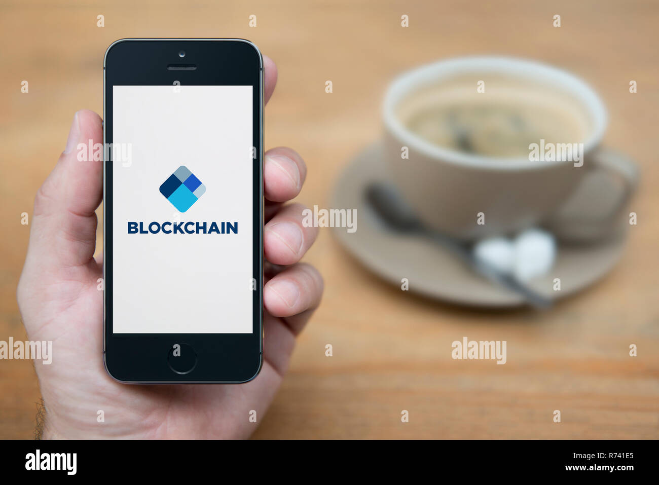 Un uomo guarda al suo iPhone che visualizza il logo Blockchain (solo uso editoriale). Foto Stock