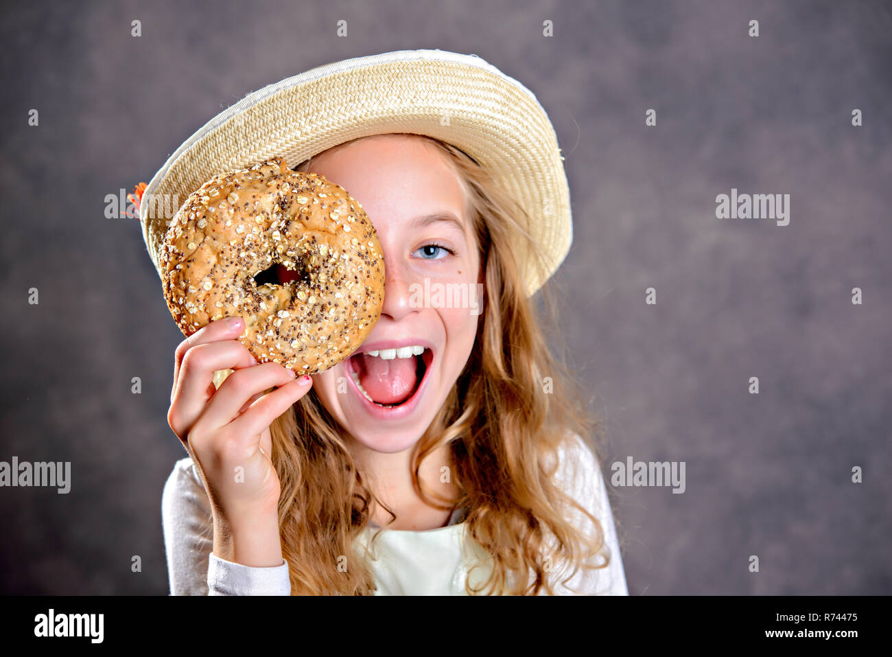 Ragazza bionda con il cappello di paglia di guardare attraverso una grande bagel Foto Stock