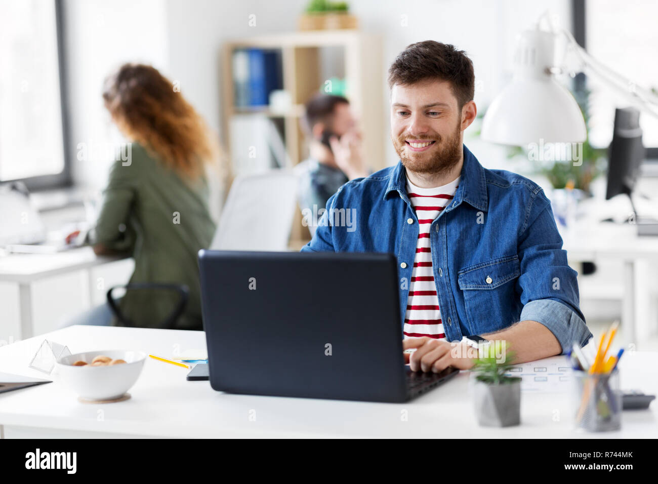 Sorridente uomo creativo con il computer portatile lavorando in ufficio Foto Stock