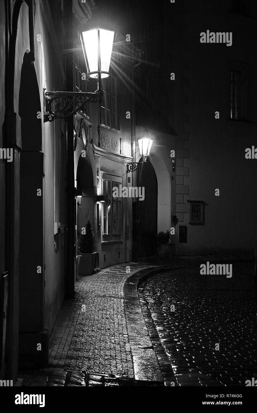 Un misterioso vicolo di Praga in una notte piovosa. Due luci di strada su con i riflessi di luce sull'acciottolato. Verticale, bianco e nero. N. persone. Foto Stock