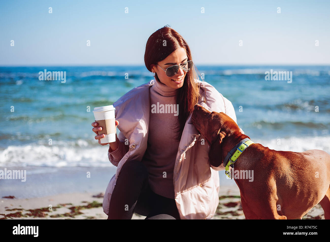Elegante metà donna adulta accovacciato sulla spiaggia come accarezzare il suo cane, Odessa, Odeska, Oblast di Ucraina Foto Stock