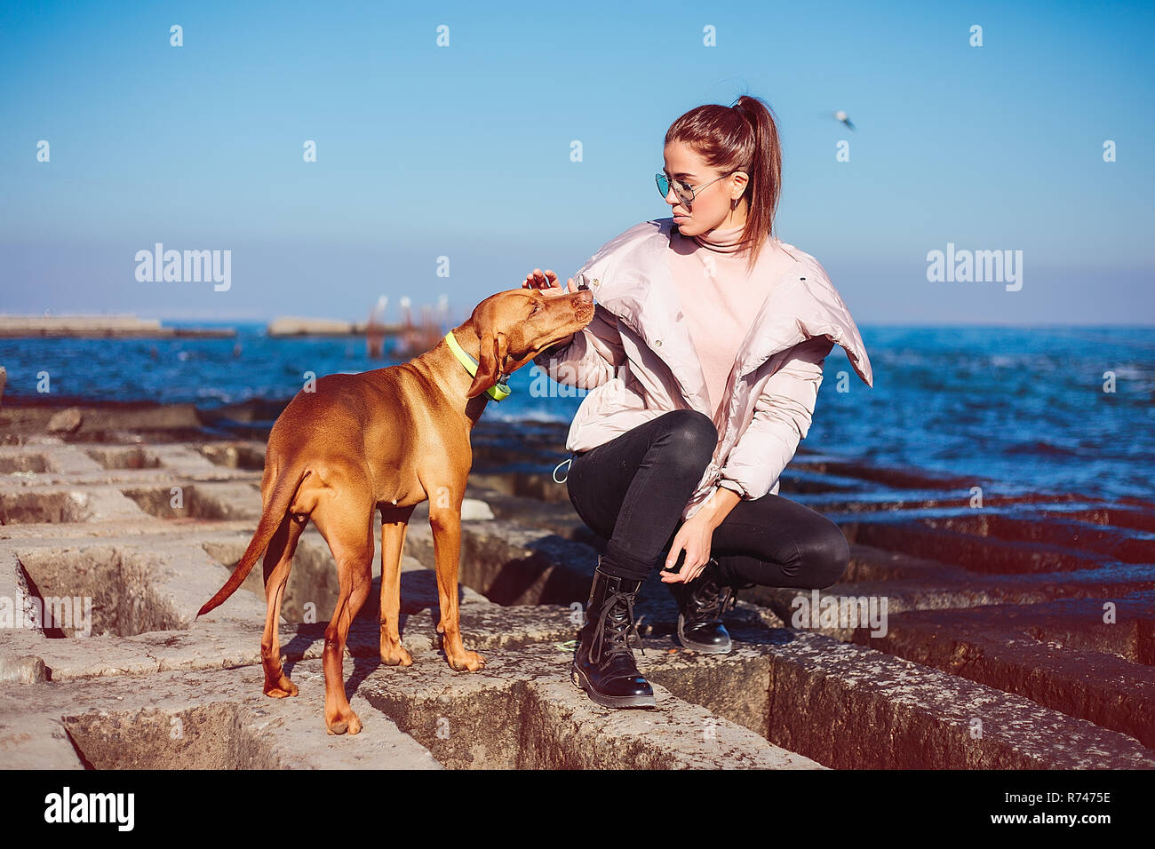 Elegante metà donna adulta accovacciato sulla difesa del mare come accarezzare il suo cane, Odessa, Odeska, Oblast di Ucraina Foto Stock
