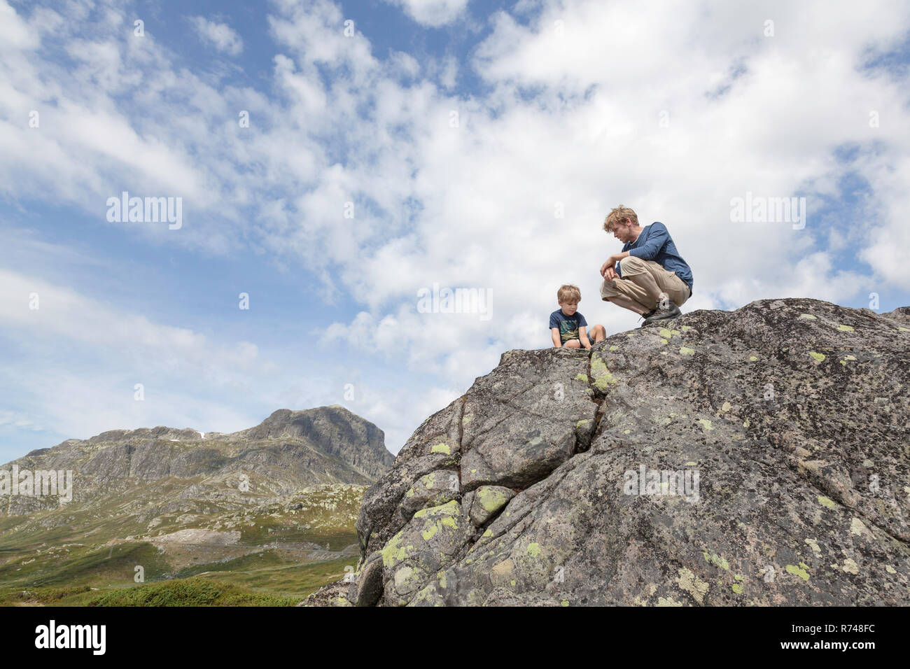Ragazzo e padre accovacciato sulla parte superiore di formazione di roccia, a basso angolo di visione, Oppland, Nord-Trondelag, Norvegia Foto Stock