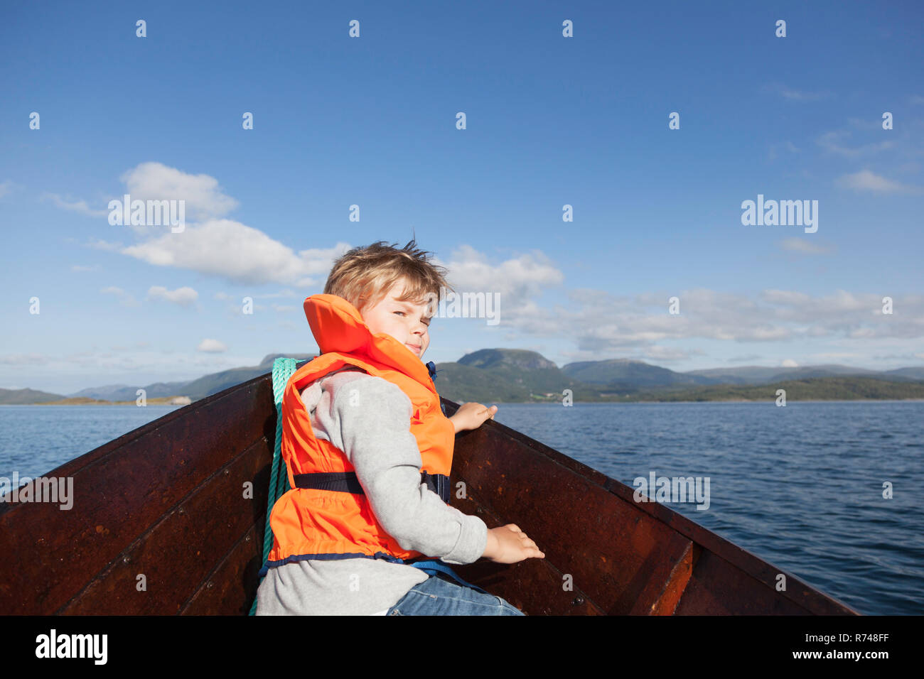 Ragazzo che guarda indietro dalla parte anteriore della barca a remi, Aure, More og Romsdal, Norvegia Foto Stock
