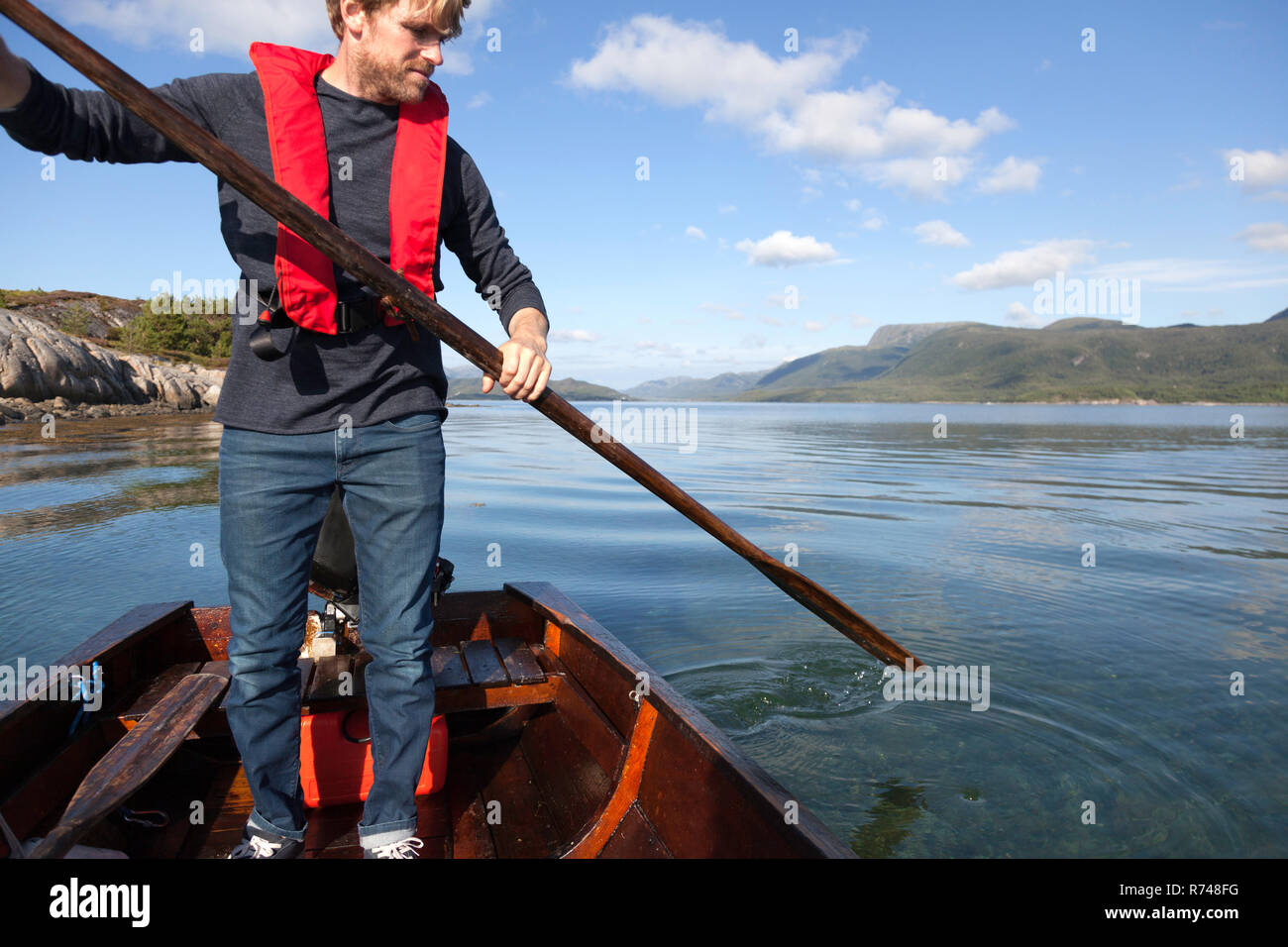 Uomo maturo in piedi fino a utilizzare remo in barca a remi, Aure, More og Romsdal, Norvegia Foto Stock