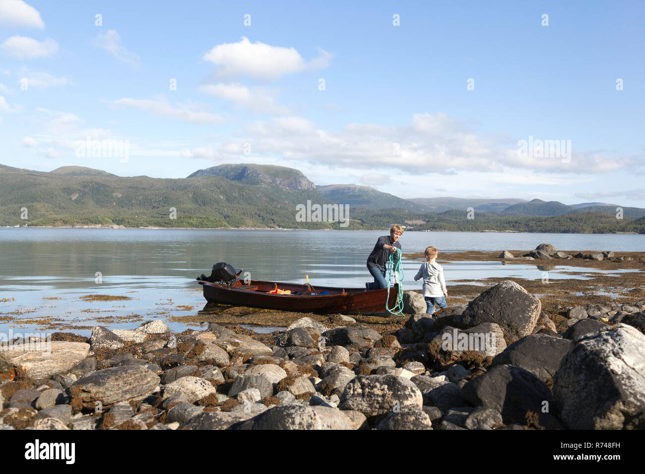 Uomo maturo che passa la fune al figlio da barca a remi, Aure, More og Romsdal, Norvegia Foto Stock