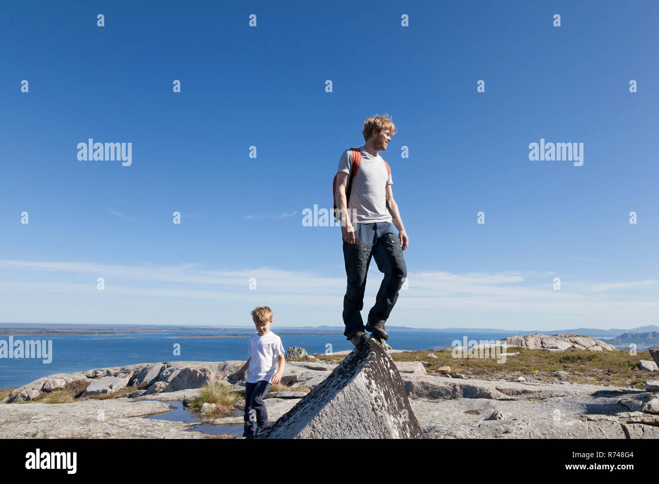 Ragazzo e padre guardando fuori dalla parte superiore della formazione di roccia oltre il paesaggio, Aure, More og Romsdal, Norvegia Foto Stock