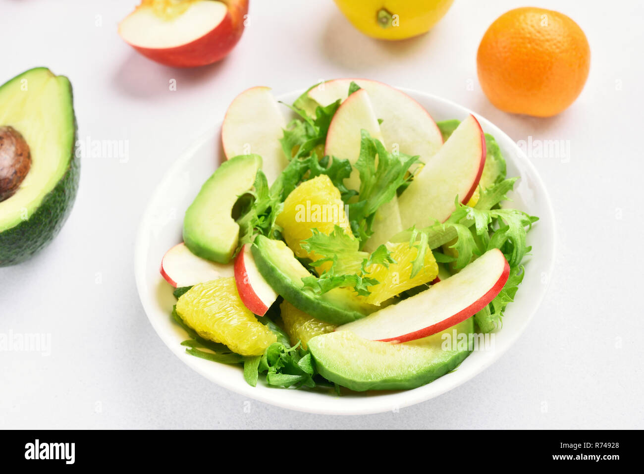 Insalata con le mele rosse, avocado, fettine di arancia su pietra bianca dello sfondo. Una sana dieta alimentare. Cucina naturale Foto Stock
