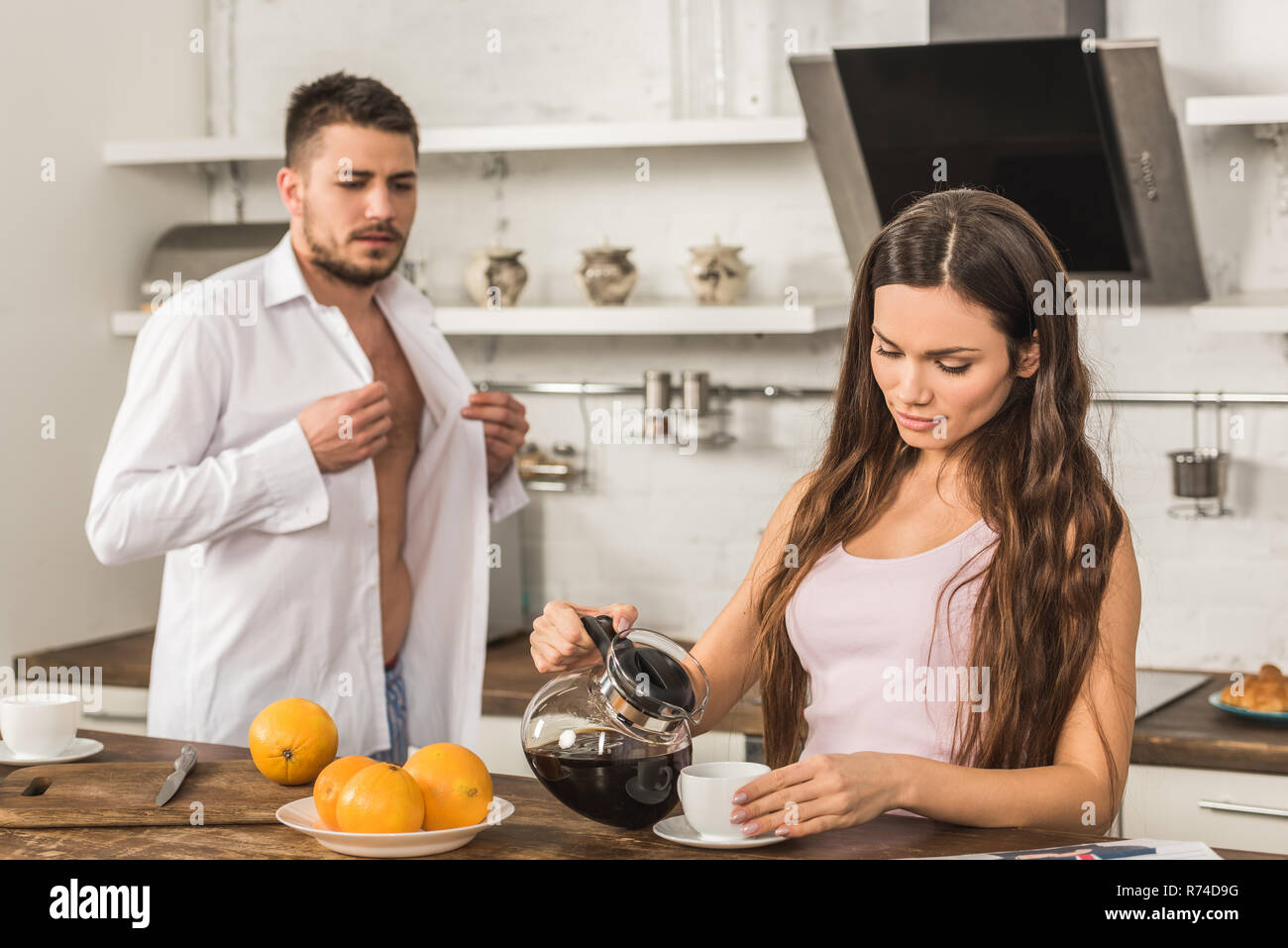 Fidanzato abbottonatura shirt e fidanzata versando il caffè nella tazza a casa, ruoli sociali concept Foto Stock