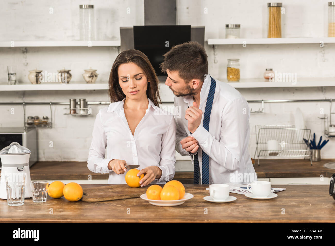 Fidanzato abbottonatura bracciale e ragazza il taglio di arance in cucina, ruoli sociali concept Foto Stock