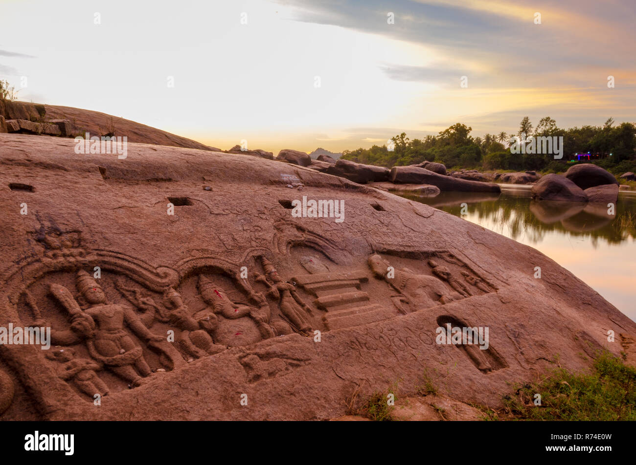 Sculture di divinità Indù su una roccia accanto al fiume Tungabhadra visto durante il tramonto di Hampi, Karnataka, India. Foto Stock