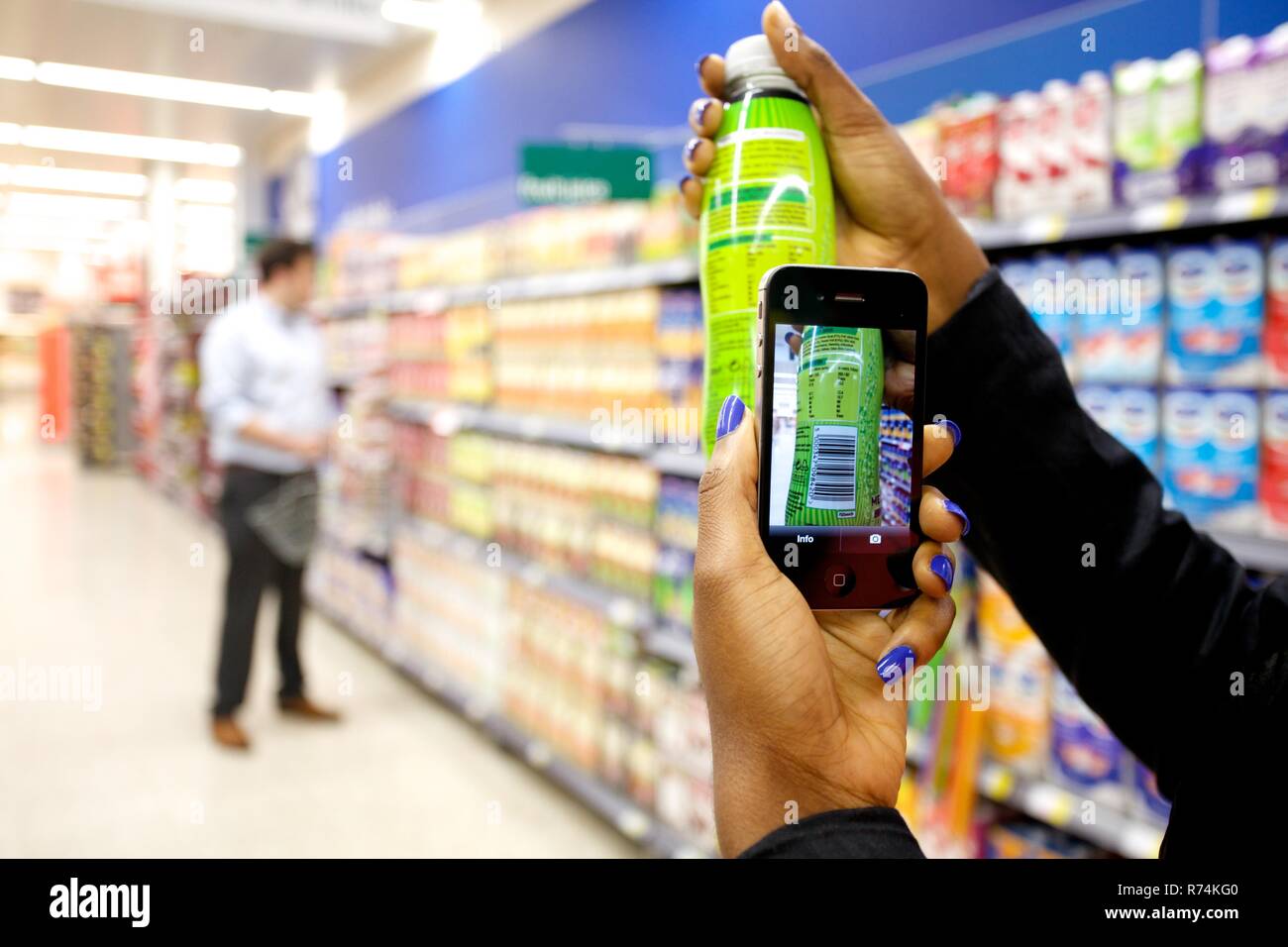 Carrello utilizzando un telefono intelligente per eseguire la scansione dei codici a barre dei beni di consumo in un supermercato Foto Stock