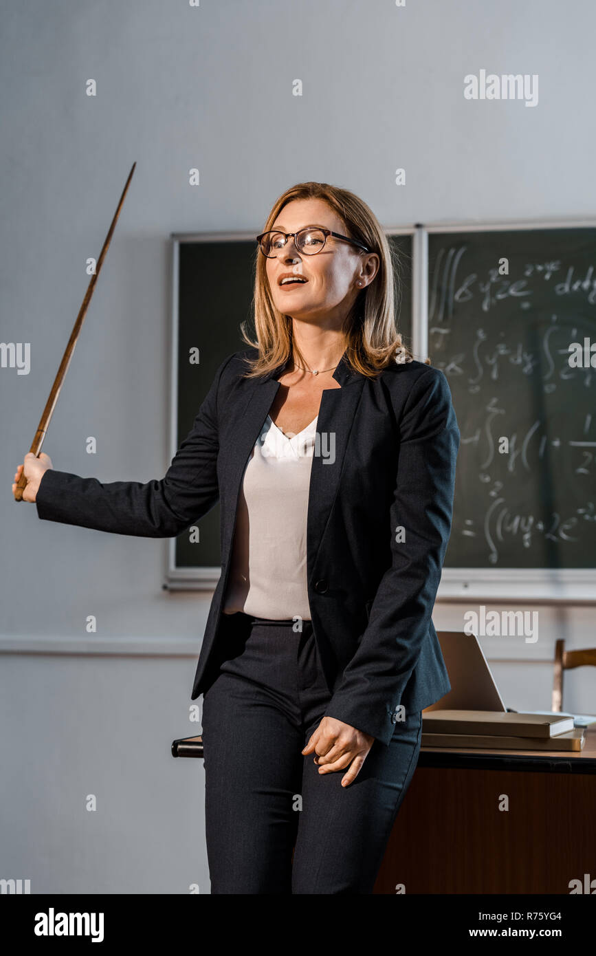 Insegnante femmina con puntatore in legno spiegando equazioni matematiche in aula Foto Stock