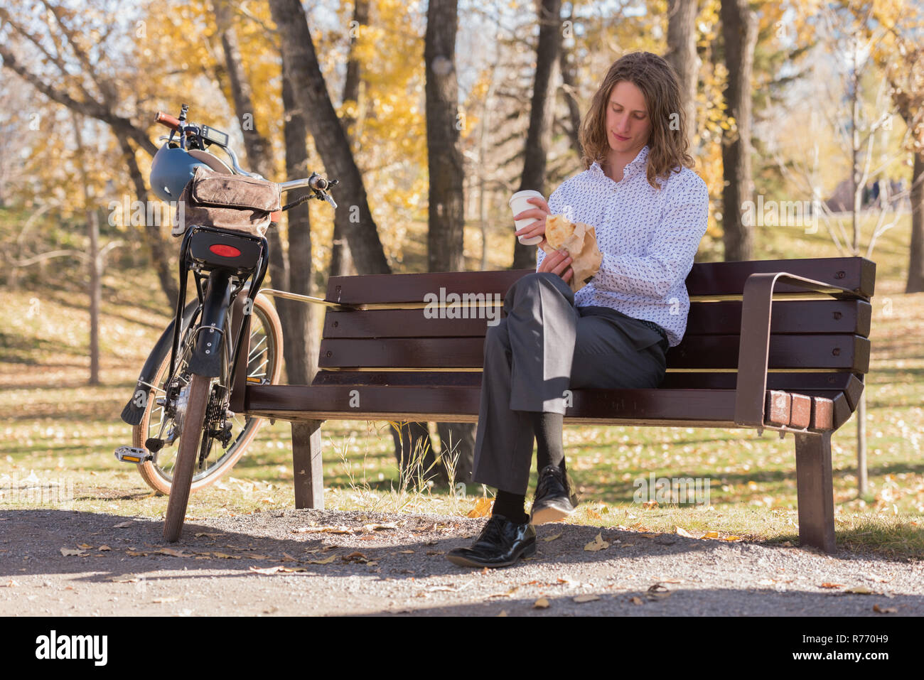 L uomo un caffè mentre è seduto su una panchina nel parco Foto Stock
