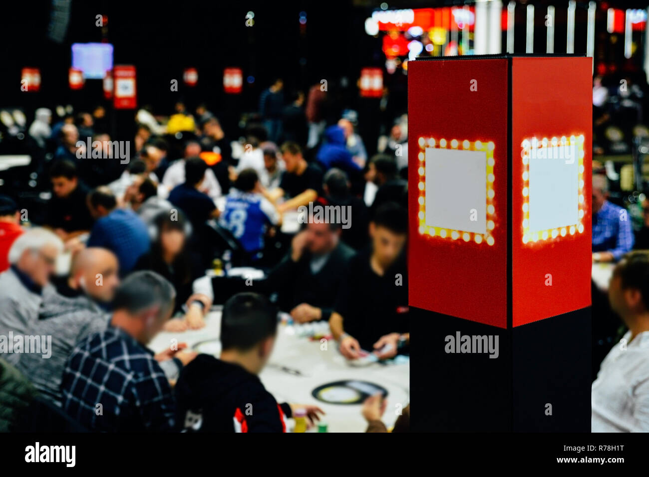 Vista sfocati di grandi poker multi-tavolo torneo. I giocatori seduti al tavolo e i concessionari che trattano le carte. Foto Stock