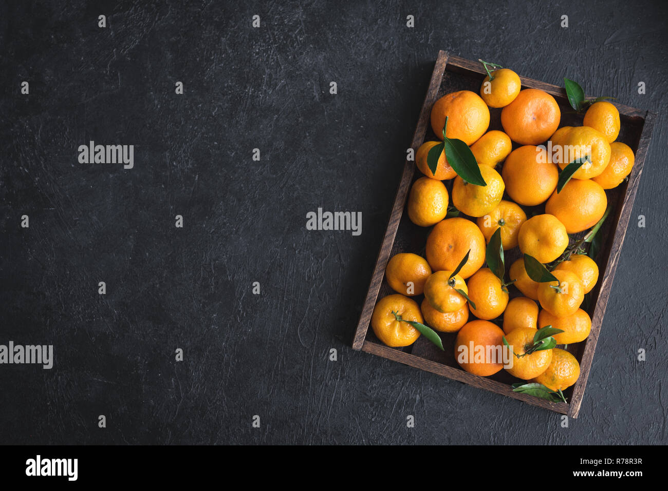 Tangerini (arance, clementine, agrumi) con foglie verdi nella casella su sfondo nero, copia dello spazio. Foto Stock